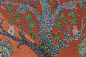 Wat Xieng Thong temple in Luang Prabang, Laos. Detail of the famous tree of life mosaic of the back wall of the sim, in colored glass on a dark red background.